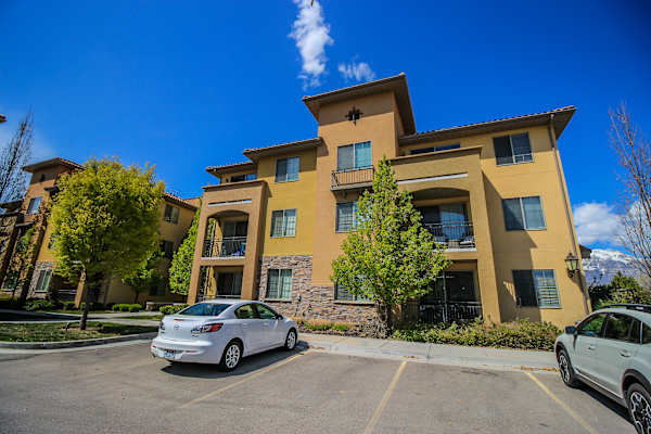 A silver car is parked in a parking lot in front of a tan apartment building at Siena Villas Apartments, Utah